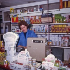 J Mace's mum behind shop counter, 1970s. | Photo: Edward Mace